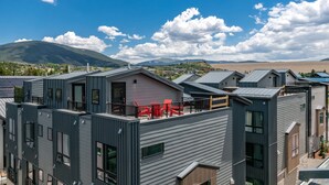 A modern building with multiple units, large windows, and a balcony with red chairs. - Fourth Street Crossing Traverse Townhome: Stylish Retreat (Silverthorne)
