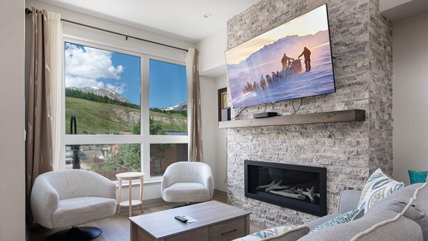A living room with a large window, a fireplace, a flat-screen TV, and a sofa. - Fourth Street Crossing Traverse Townhome: Stylish Retreat (Silverthorne)