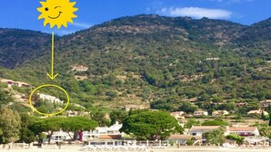 Un pueblo costero con playa, casas y una montaña al fondo.