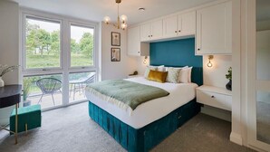 A modern bedroom with a large bed, white cabinets, a teal accent wall, and a view of greenery outside. - Host & Stay | Scarborough View Luxury Apartment (Scarborough)