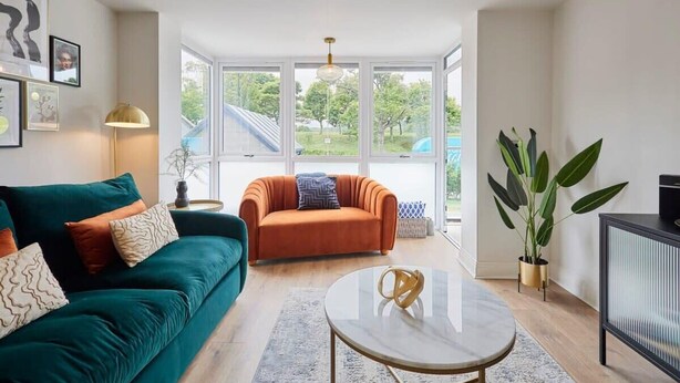 A living room with a teal sofa, an orange armchair, a round coffee table, and a large window offering a view of the outdoors. - Host & Stay | Scarborough View Luxury Apartment (Scarborough)