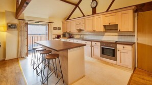 A kitchen with wooden beams, a large island with stools, and a clock on the wall. - Host & Stay | Widger Mews Apartment (Malton)
