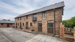 A brick building with multiple windows and doors, a gravel driveway, and a parked car. - Host & Stay | Widger Mews Apartment (Malton)