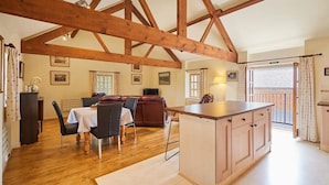 A spacious kitchen with wooden beams, a dining area with a table and chairs, and a view of the outside. - Host & Stay | Widger Mews Apartment (Malton)