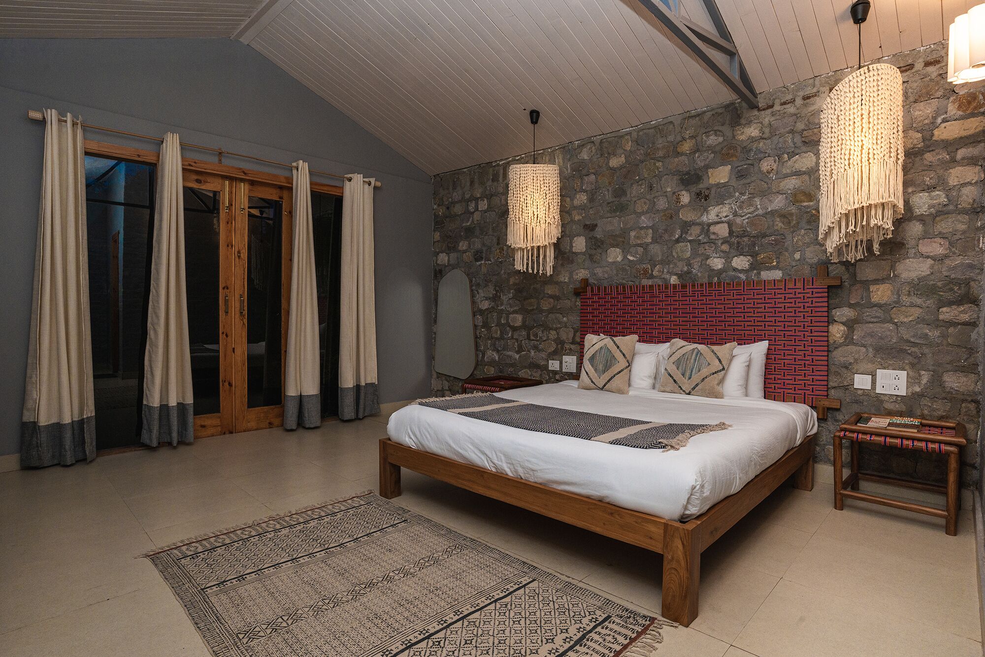 Ein Schlafzimmer mit Steinwand, einem Holzbett, einem gemusterten Teppich und einem Nachttisch mit Lampe.