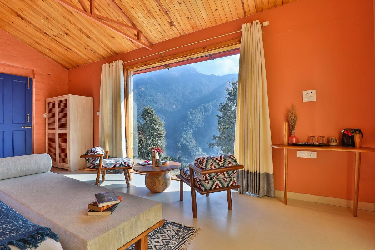 Une chambre avec un lit, deux chaises, une table et une vue sur les montagnes, visible à travers de grandes fenêtres.