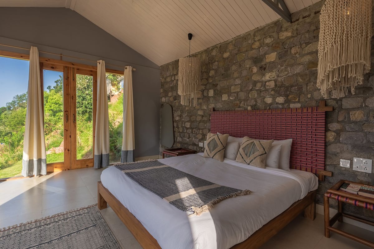 Une chambre avec un mur en pierre, un cadre de lit en bois et une vue sur la verdure.