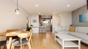 A modern living room with a wooden dining table, grey sofa, and white coffee table. - Coogee Beach Escape | Pool & Balcony (Randwick)