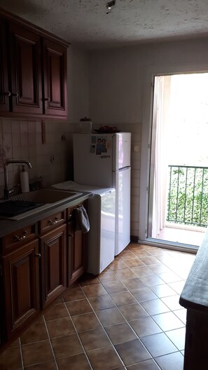 Cozinha com armários de madeira, uma geladeira branca, uma pia e uma janela com vista para o verde lá fora.