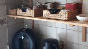 Keittiössä on hyllyjä, joilla on koreja, ruukkukasvi, vedenkeitin, leivänpaahdin ja kahvinkeitin.