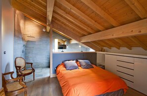 A bedroom with a sloped ceiling, a bed with orange bedding, a wooden chair, and a white wardrobe. - Chalet, fitness, hammam, balcony, fireplace or stove, parking, tv, 271m², Les 2 Alpes (Les Deux Alpes)