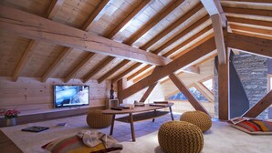 A cozy attic room with a wooden ceiling, a television, a table, and two knitted poufs. - Chalet, 300m from ski slopes, fitness, hammam, balcony, fireplace or stove, parking, tv, 271m² (Les Deux Alpes)