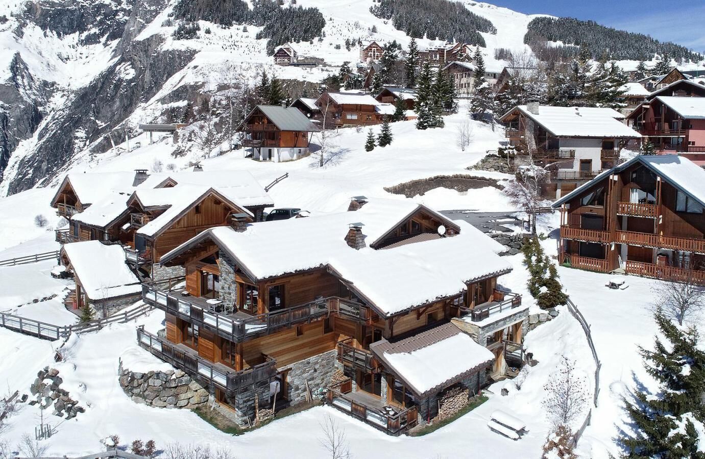Un chalet de montagne enneigé, composé de plusieurs cabanes en bois, dotées de fondations en pierre, et d’un bâtiment central avec un balcon.