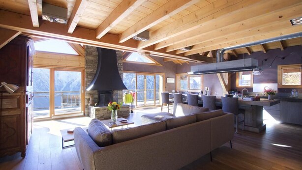 A spacious living area with a stone fireplace, wooden beams, and large windows offering mountain views. - Chalet, 300m from ski slopes, fitness, hammam, balcony, fireplace or stove, parking, tv, 271m² (Les Deux Alpes)