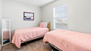 Een slaapkamer met twee bedden, een plafondventilator, een raam met zonwering en een lijst met een afbeelding.
