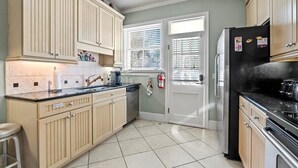 Una cocina con gabinetes color beige, un refrigerador negro y piso de baldosas.