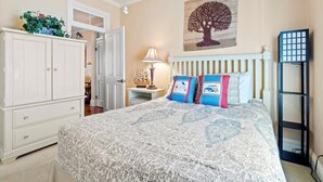 Un dormitorio con cama, armario, mesita de noche, lámpara, una obra de arte en la pared y estantería.