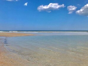 A beach with clear water and a sandy shore under a blue sky with clouds.