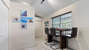 Un coin repas avec une longue table et quatre chaises, une porte blanche et un mur orné de tableaux.