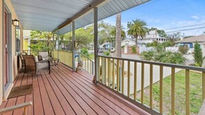 Une véranda couverte avec un plancher en bois, des rampes en métal et du mobilier d’extérieur.