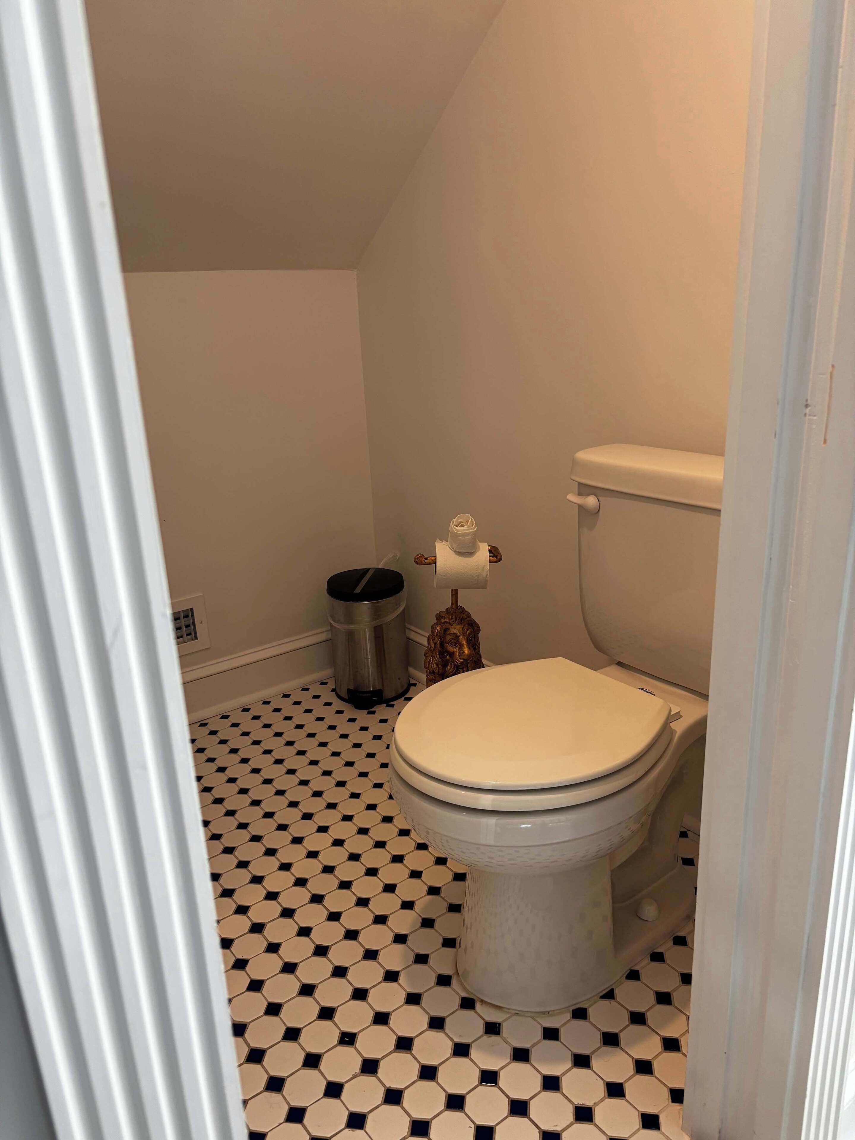 A bathroom with a toilet, a trash can, and a tissue holder on the wall.