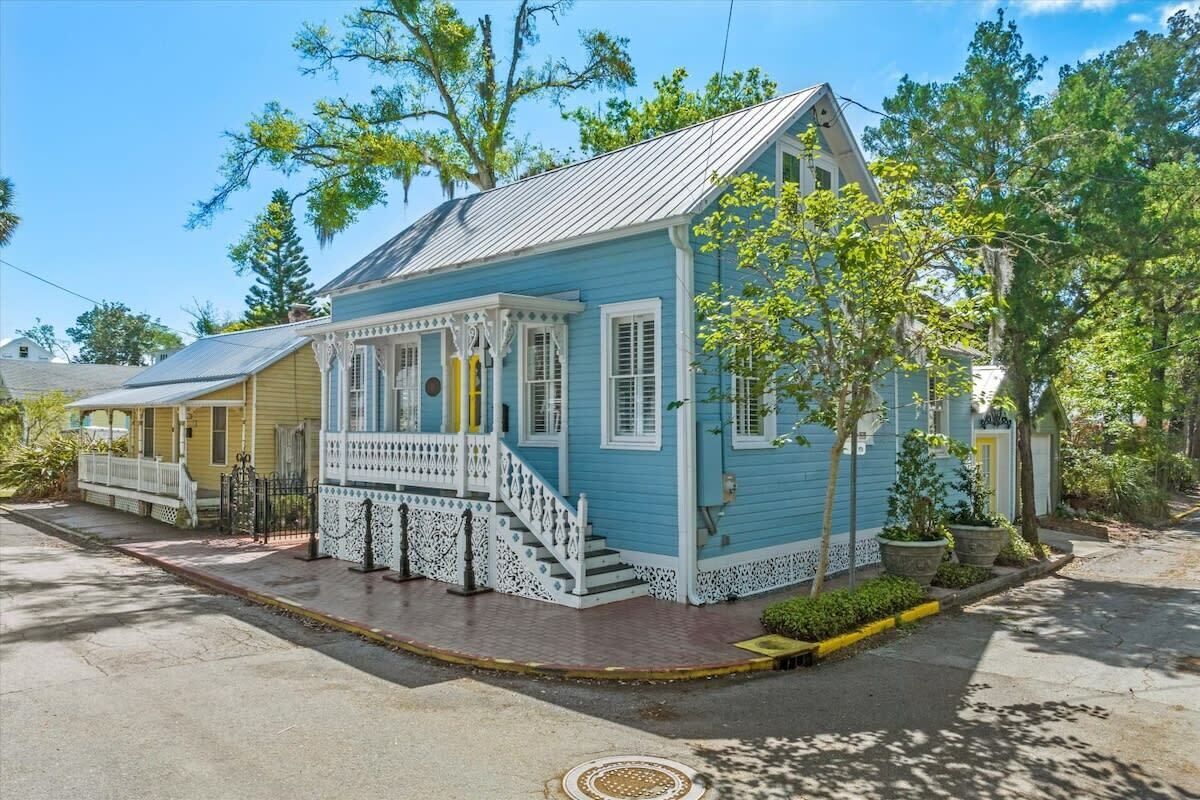 A two-story house with a porch, a small staircase, and a front yard with trees and a sidewalk.
