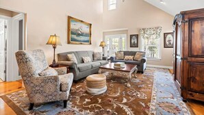A spacious living room with a high ceiling, a large window, and a ceiling fan.