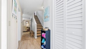 A hallway with wooden flooring, a staircase, and a shelf with folded towels. - Beach Townhome - Pool, Patio & Direct Beach Path (St. Augustine)