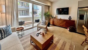 Tilava olohuone, jossa on suuri ikkuna, kattotuuletin, litteänäyttöinen televisio ja moderni keittiöalue.