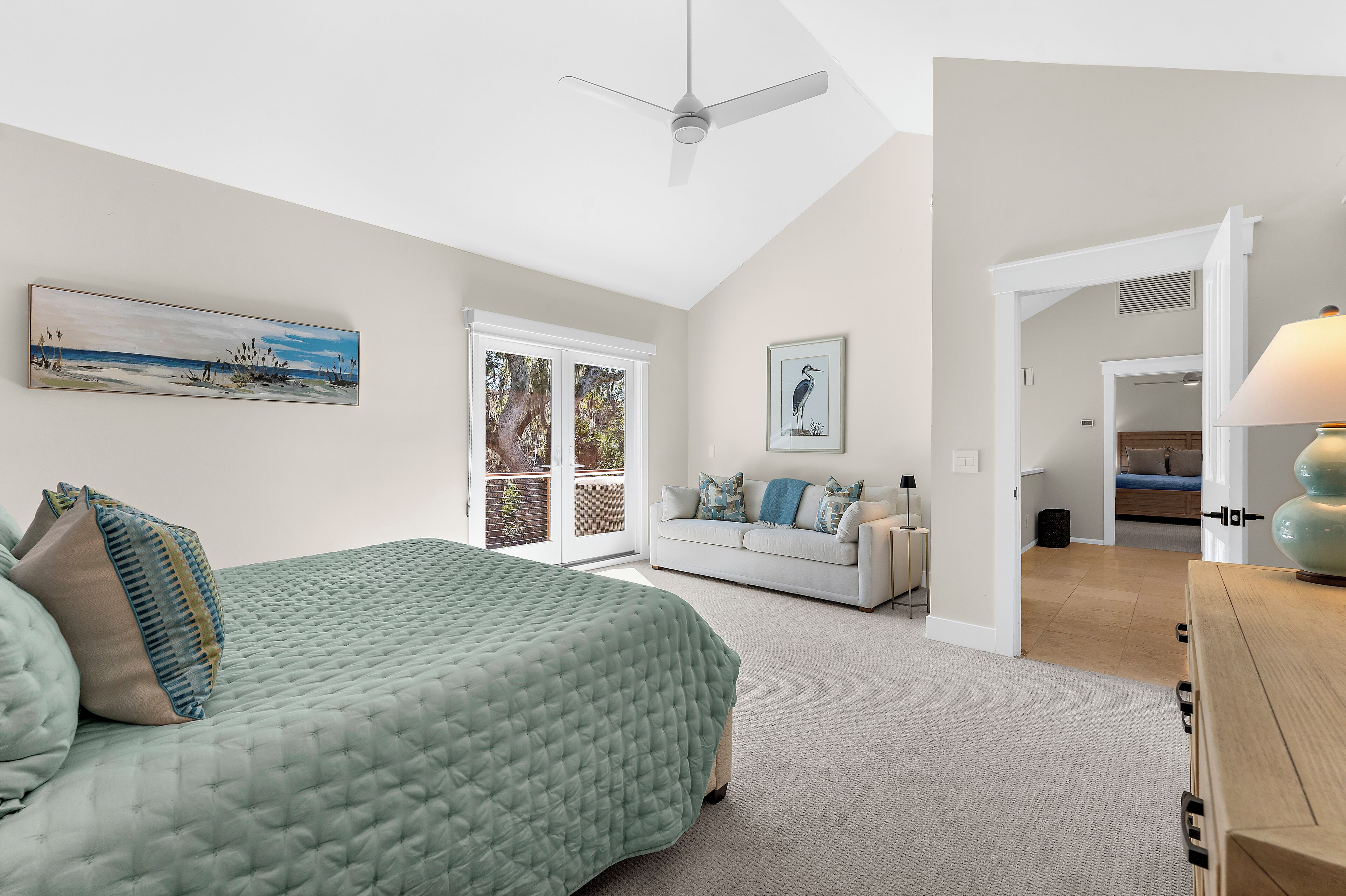 A bedroom with a bed, a sofa, a ceiling fan, and a painting on the wall.