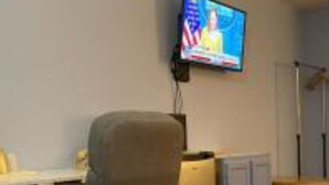A room with a desk, chair, television, and a small cabinet. - Lake Country Inn  (Trinity)
