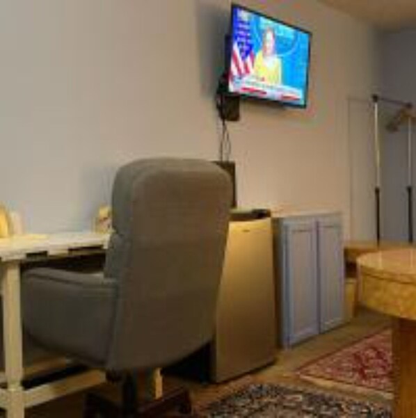 Una habitación con escritorio, silla, televisión y un mueble pequeño.