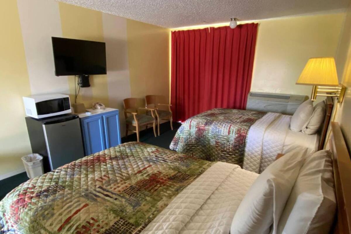 A hotel room with two beds, a TV, a desk with a microwave, and a red curtain.
