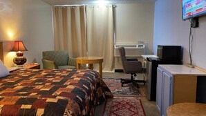 A hotel room with a bed, a desk, a chair, a television, and an air conditioning unit. - Lake Country Inn  (Trinity)