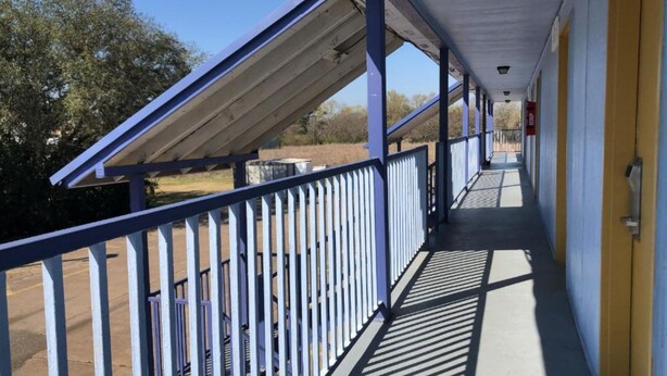 A covered outdoor corridor with a metal railing, a fire extinguisher, and a clear view of the surrounding landscape. - Lake Country Inn  (Trinity)