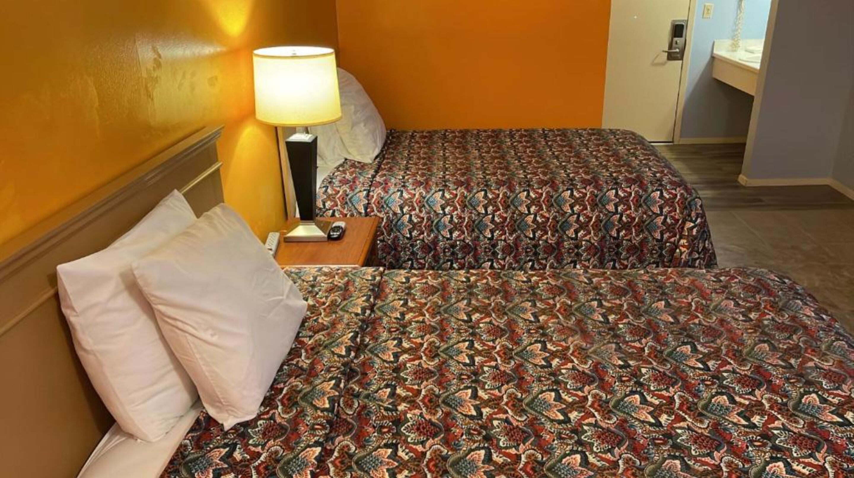 Een hotelkamer met twee bedden, een nachtkastje met een lamp, en een badkamer op de achtergrond.