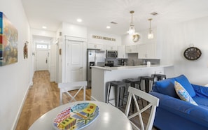 A modern kitchen with white cabinets, a stainless steel refrigerator, and a bar area with stools.