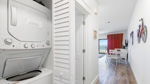 A laundry area with a washing machine and dryer, a dining area with a table and chairs, and a view of the sea through a balcony. - Views of the Gulf, Private Beach Access, & Bikes (Santa Rosa Beach)