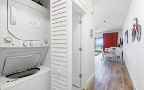 A laundry area with a washing machine and dryer, a dining area with a table and chairs, and a view of the sea through a balcony.