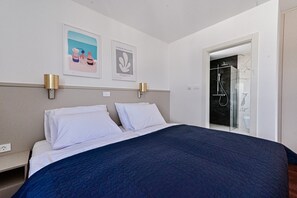 Habitación de hotel con una cama grande, dos lámparas fijadas a la pared, una obra de arte enmarco y zona de ducha con mampara de vidrio.