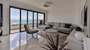 A spacious living room with a large sliding glass door leading to a balcony with a sea view.