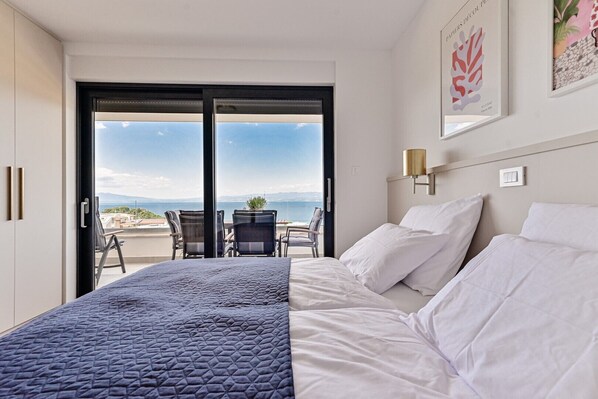 Habitación de hotel con cama, balcón con sillas y vista al mar.