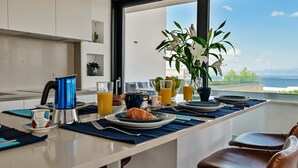 Ein Frühstücksbuffet mit Kaffeemaschine, Croissants und Orangensaft auf einem Tisch mit Blick aufs Meer.