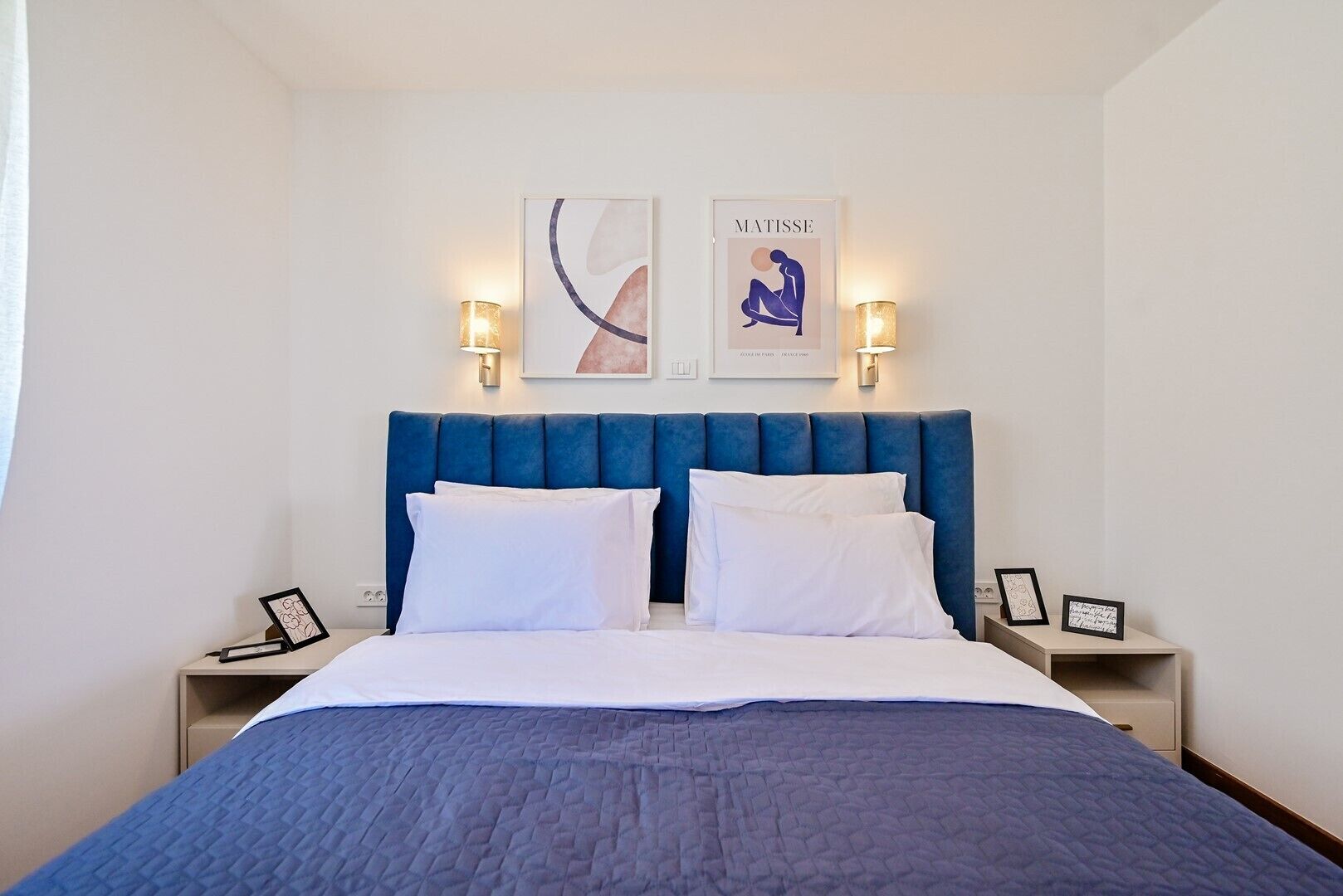 Habitación de hotel con una cama grande, dos lámparas fijadas a la pared y dos cuadros enmarcados.