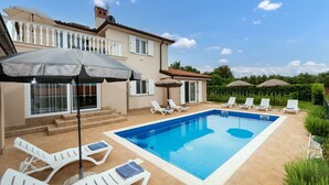 A swimming pool with lounge chairs and umbrellas, a staircase leading to a balcony, and a garden area with greenery. - Lovely Villa Buroli with swimming pool, jacuzzi and sauna (Buroli)
