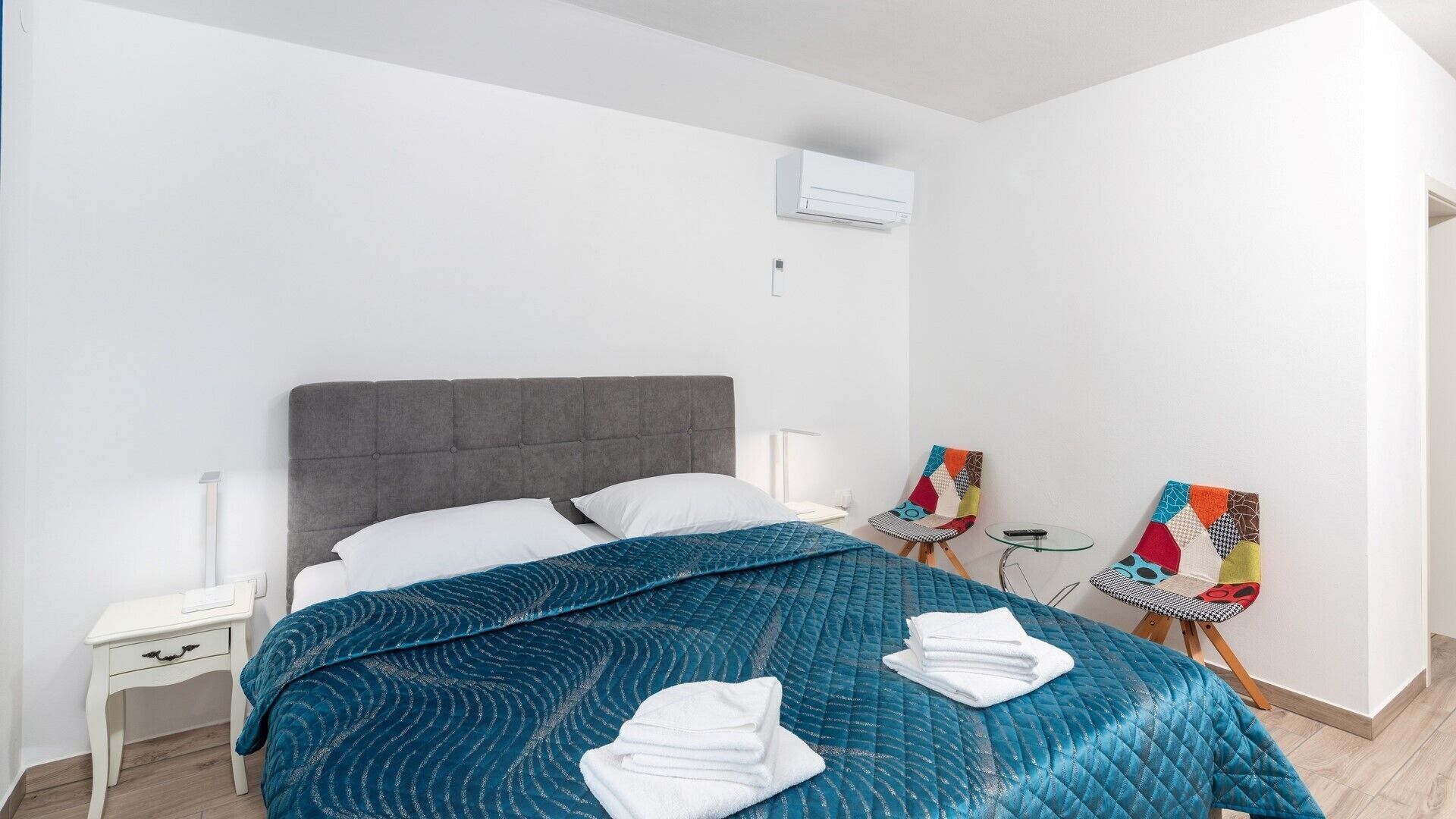 Une chambre à coucher comprenant un lit, une table de chevet, une chaise, une petite table et un appareil de climatisation.