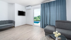 A modern living room with a grey sofa, a flat-screen TV, and a glass coffee table with a vase of flowers. - Lovely Villa Buroli with swimming pool, jacuzzi and sauna (Buroli)
