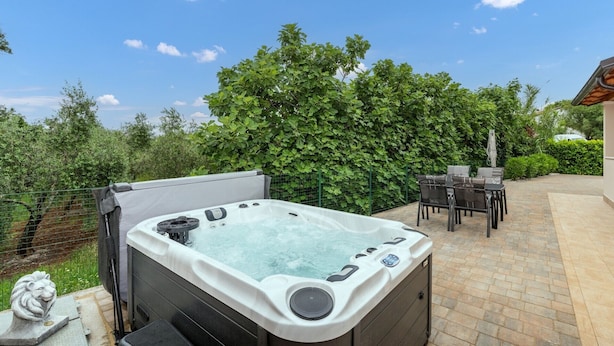 A hot tub in a backyard with a patio table and chairs, surrounded by greenery. - Lovely Villa Buroli with swimming pool, jacuzzi and sauna (Buroli)