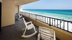 Un balcón con vista a la playa, sillas de plástico blancas y una barandilla.