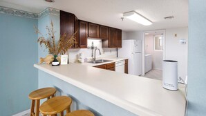 Una cocina con armarios de madera, encimera blanca y lavavajillas integrado. Hay tres taburetes de madera en la encimera.
